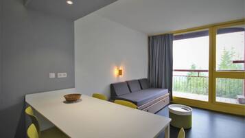 Una habitación moderna con una mesa de comedor, sillas amarillas, un sofá gris y un ventanal con vistas a zonas verdes.