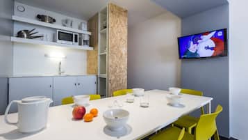 Una cocina moderna con una mesa blanca, sillas amarillas y un televisor montado en la pared.