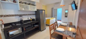 A compact kitchen with a refrigerator, microwave, and stove. There is a dining area with a table and chairs, and a TV mounted on the wall.