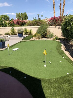 A miniature golf course with artificial grass, a putting green, and a flagstick.