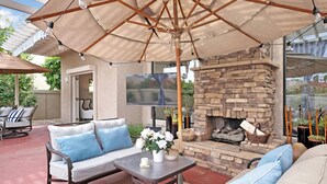 An outdoor patio with a stone fireplace, a sofa, and a table with a vase of flowers. - Large House in Lake La Quinta Community. Gated with Security Guard, Private Pool (La Quinta)