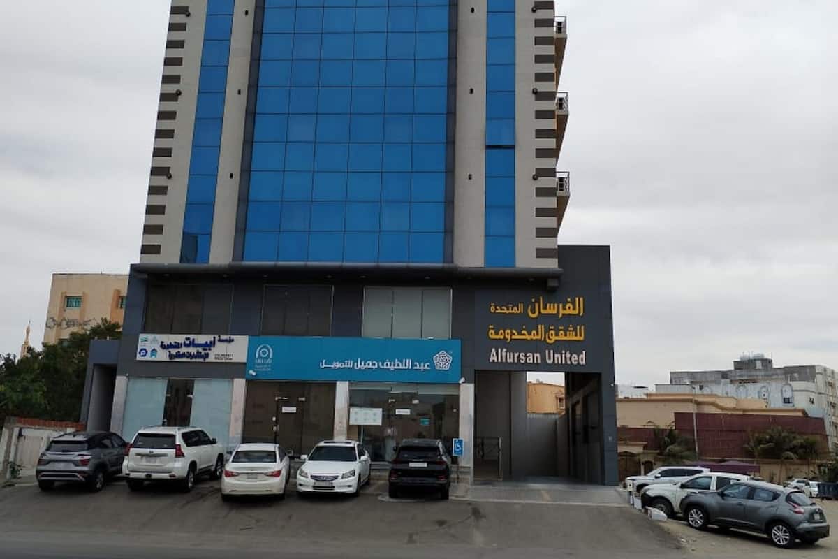A modern building with a blue glass facade, featuring signage for Alfrasan United and a nearby business.