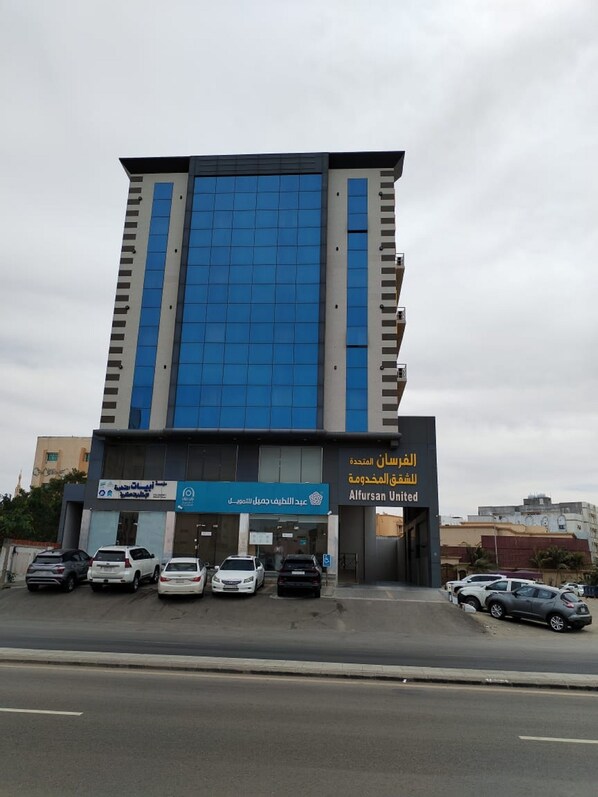 Un bâtiment moderne à la façade bleue en verre, sur lequel on peut voir des enseignes pour Alfrasan United et une entreprise située à proximité.