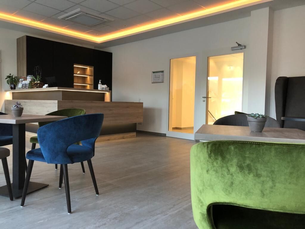 Un área de recepción moderna con un mostrador de madera, una silla azul y una silla verde.
