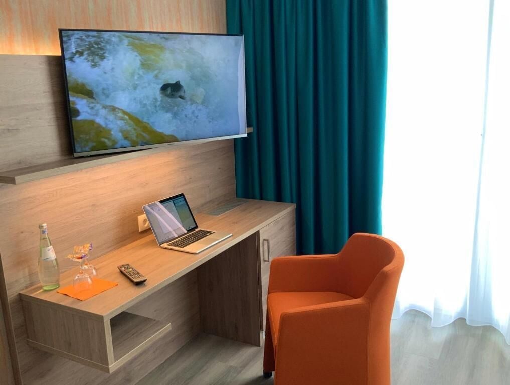 Ett modernt hotellrum med ett skrivbord i trä, en bärbar dator, en fjärrkontroll och en glasflaska.