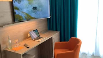 Ett modernt hotellrum med ett skrivbord i trä, en bärbar dator, en fjärrkontroll och en glasflaska.