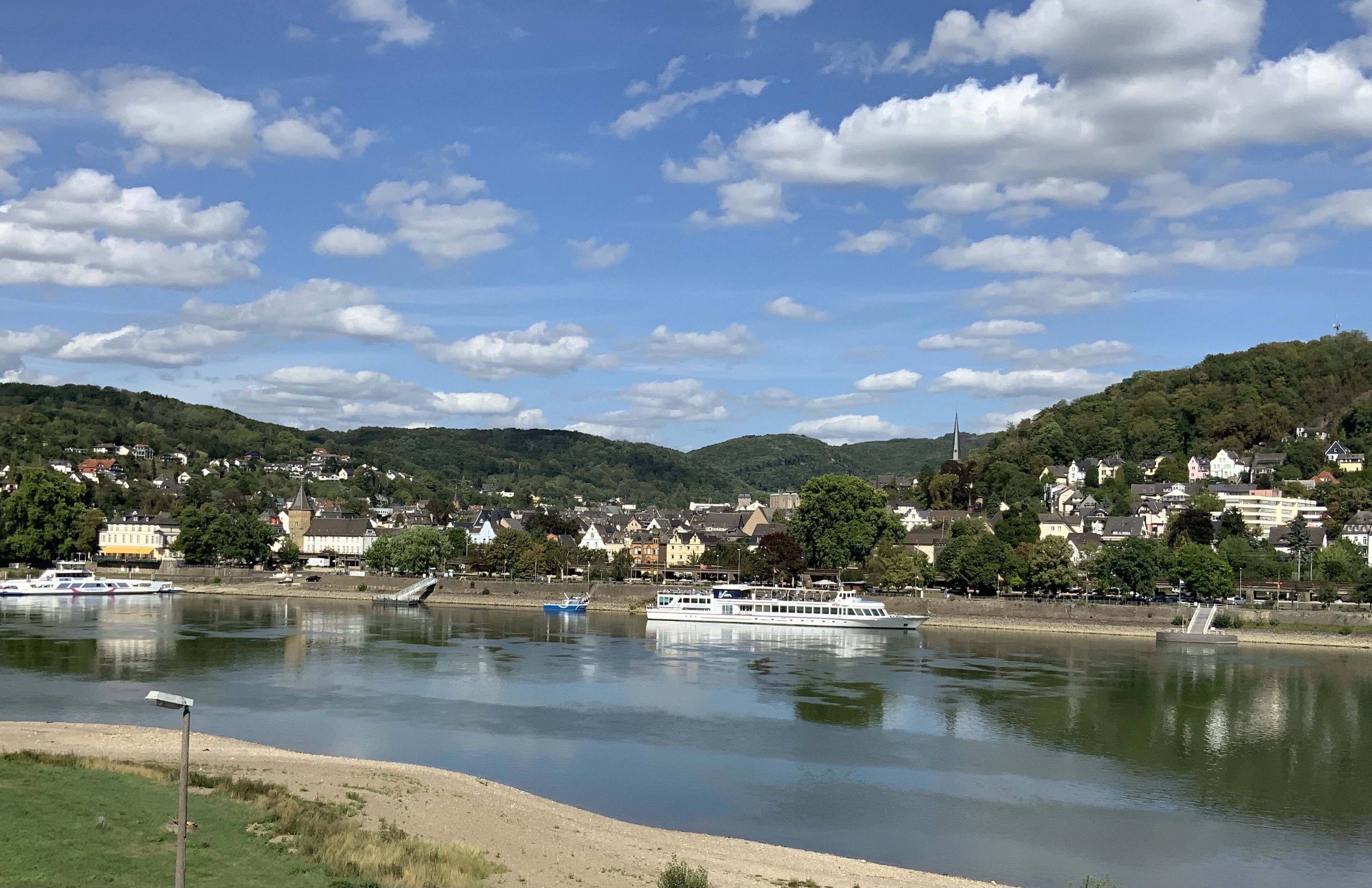 Un río con barcos, un pueblo en la orilla opuesta y colinas al fondo.
