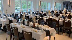 A spacious dining area with multiple tables set for a formal event, featuring white tablecloths, dark chairs, and floral centerpieces. - RheinVilla ARTE (Remagen)