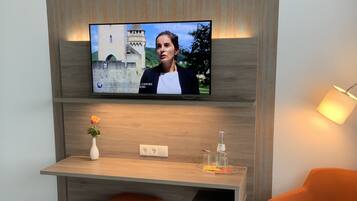 A modern room with a television mounted on a wooden wall, a small desk with a vase of flowers, and an orange chair.