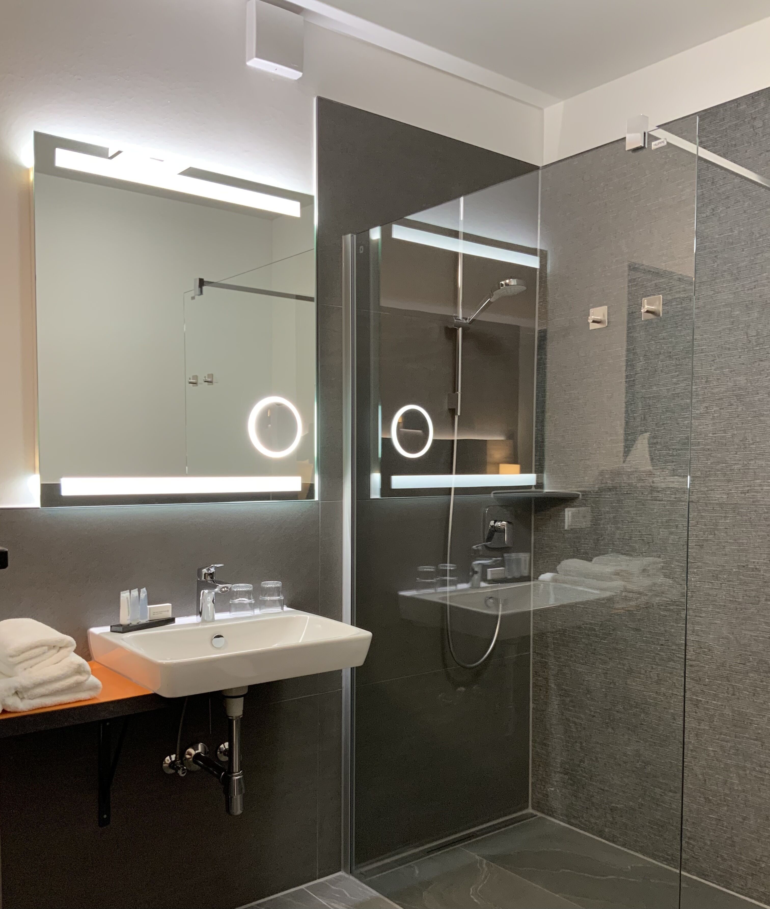 A modern bathroom with a glass-enclosed shower, a white sink, and a large mirror with integrated lighting.