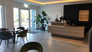 A modern reception area with a wooden reception desk, potted plants, and a seating area with chairs and a table. - RheinVilla ARTE (Remagen)