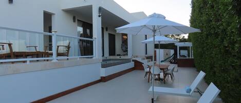 Un patio exterior moderno con mobiliario blanco, una piscina y un seto bien cuidado.