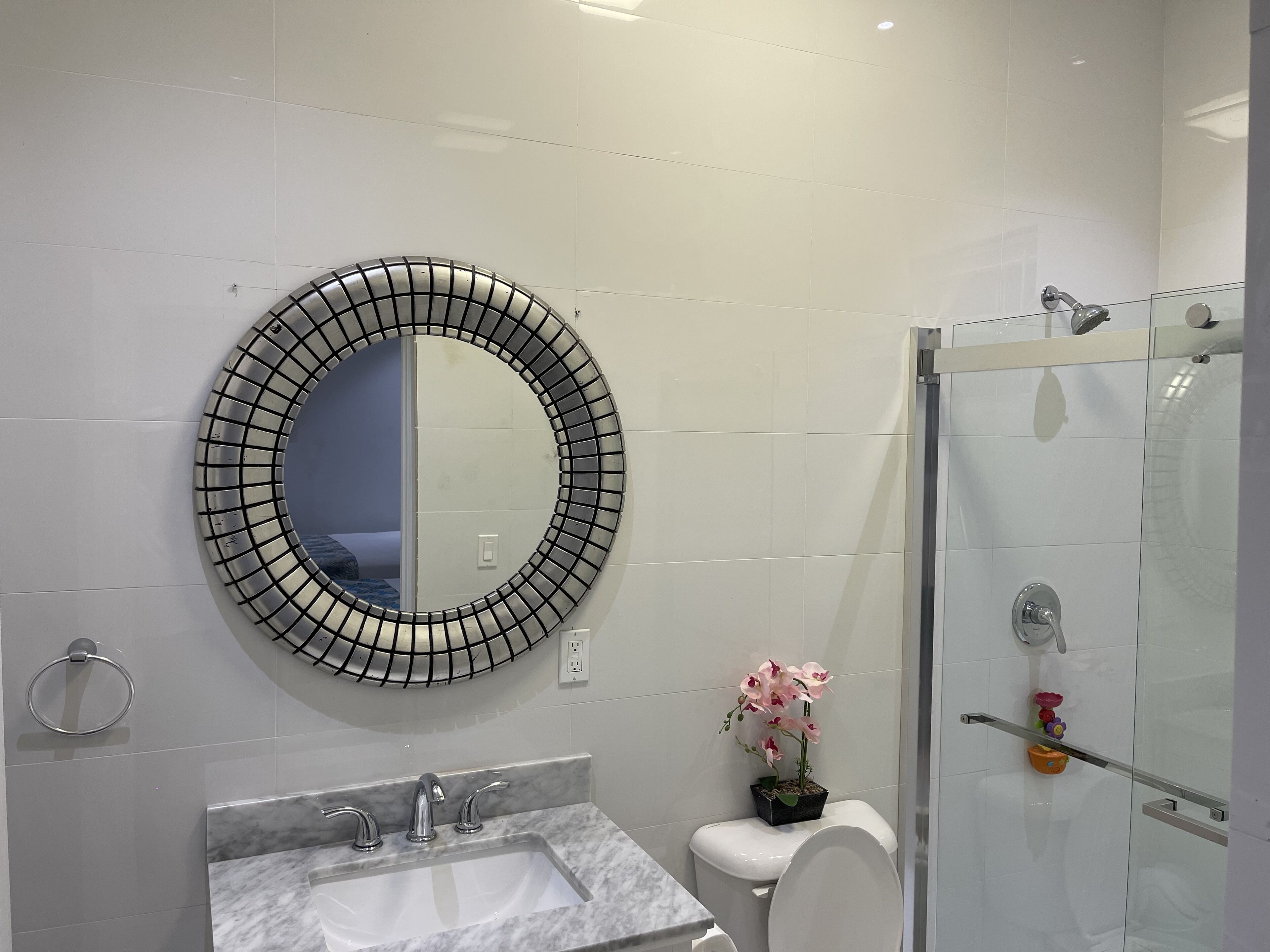 A modern bathroom with a round mirror, a toilet, a sink, and a glass shower enclosure.