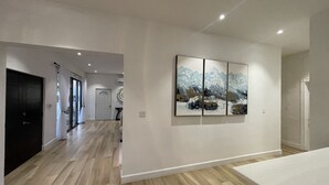 A modern hallway with wooden flooring, a black door, and a white wall with a triptych painting. - The White House TCI Guest House (Providenciales)