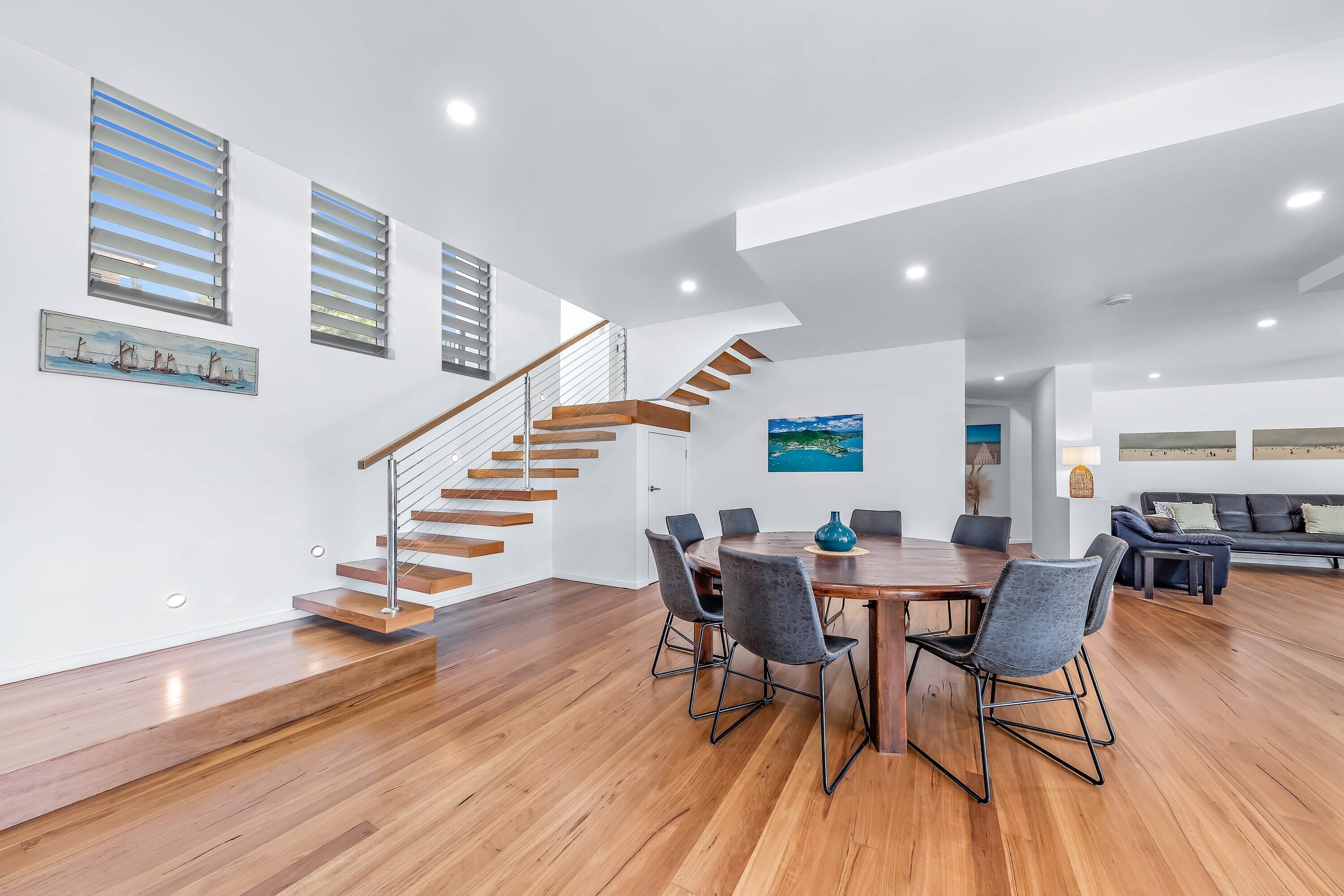 A spacious living area with a wooden staircase, a dining table with chairs, and a sofa.