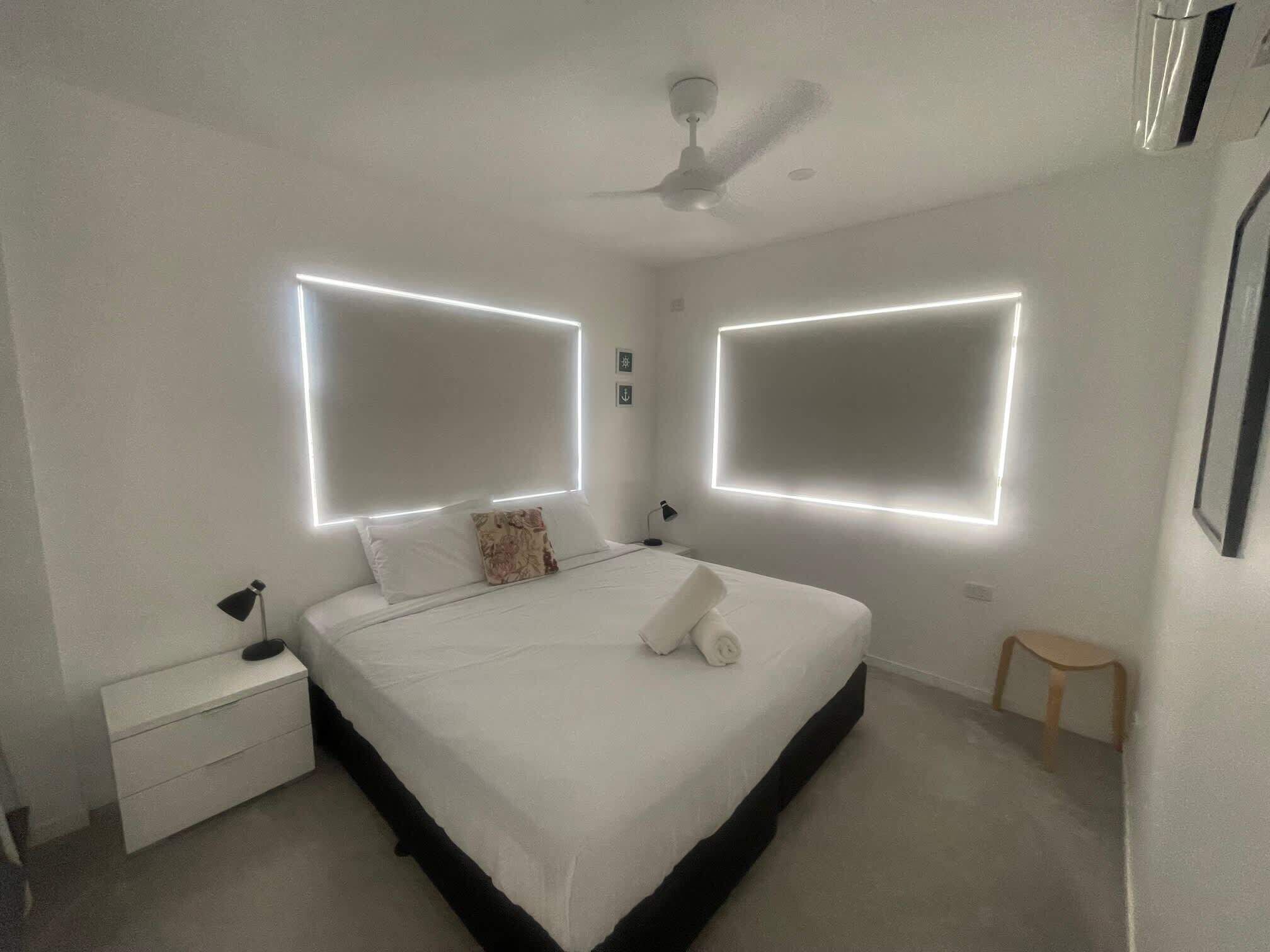 Un dormitorio moderno con una cama grande, mesitas de noche, ventilador de techo e iluminación empotrada.
