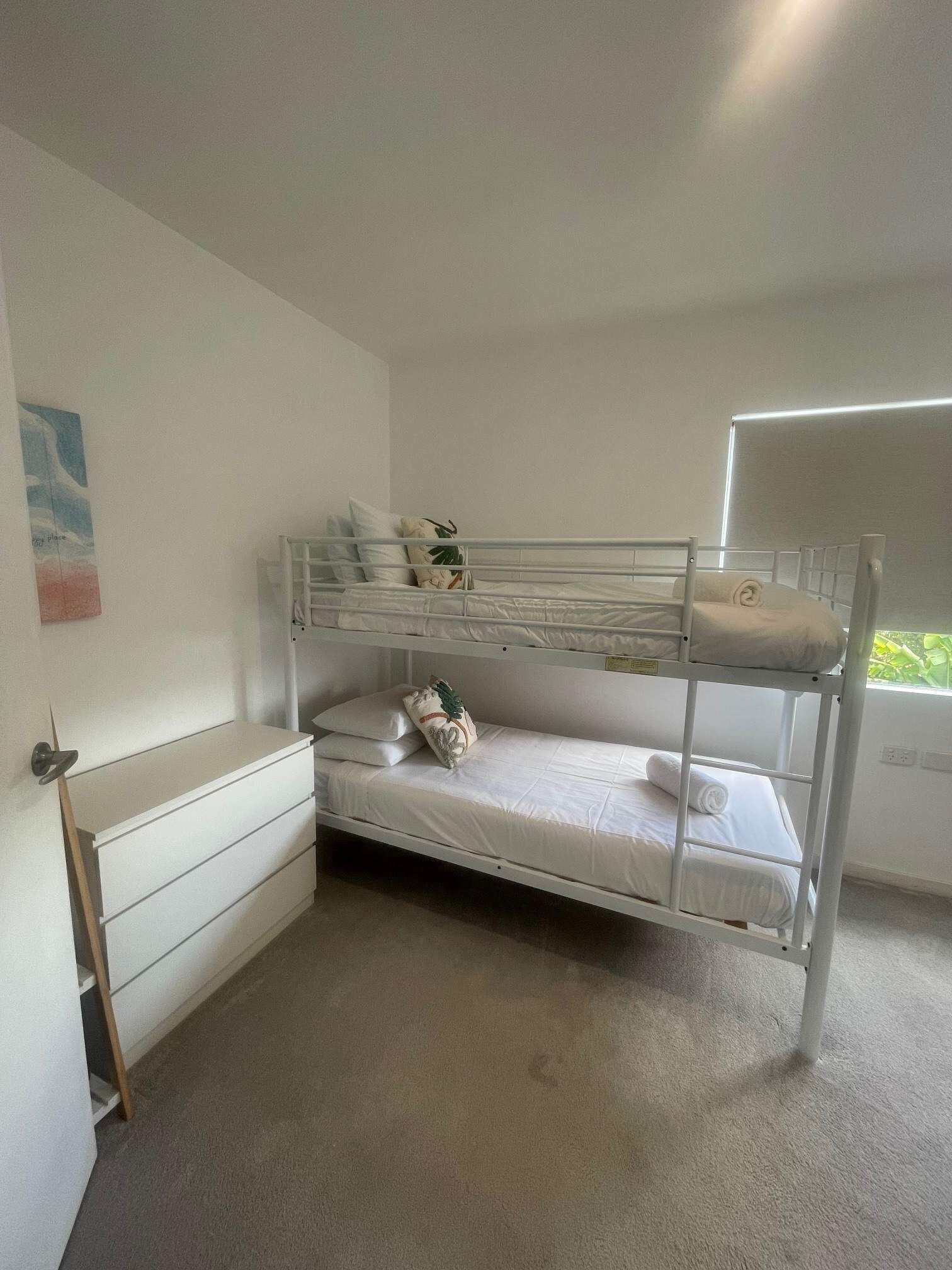 A bunk bed room with a white dresser and a small window.