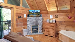 Ein gemütliches Blockhaus-Interieur mit Kamin, Holzwänden, einem Bett und Blick ins Freie.