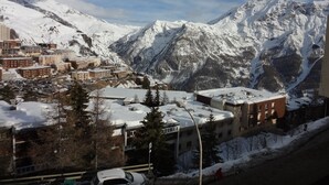 Paisagem montanhosa com picos cobertos de neve e uma cidade com edifícios e carros estacionados.