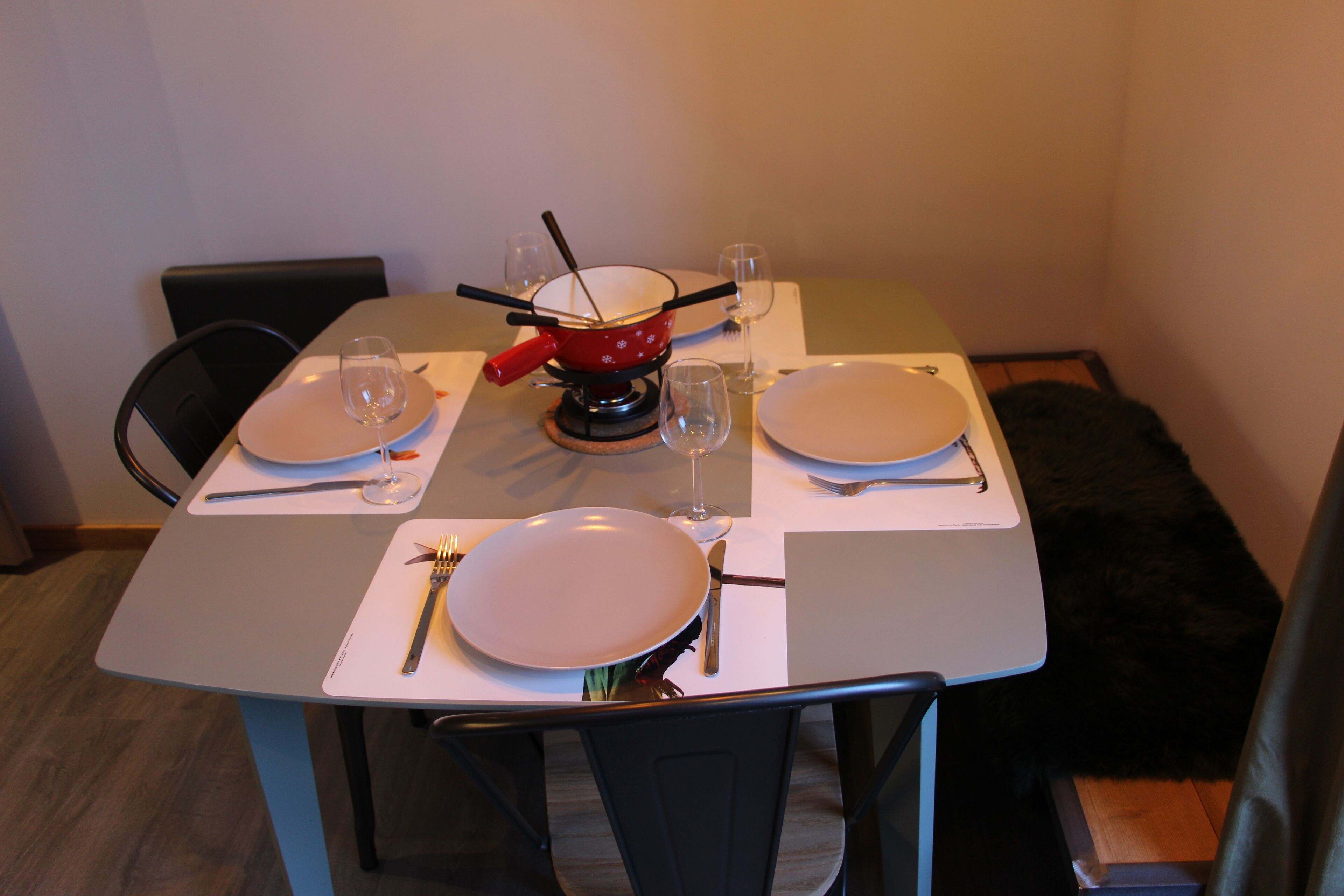 Een eettafel gedekt met borden, bestek en glazen, met een rode pot in het midden.