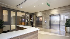 A modern reception area with a marble counter, elevators, and a glass door leading to a bathroom. - Sandton Smart Apartment Fourteen (Sandton)