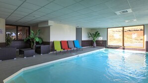An indoor swimming pool with a tiled floor, a poolside area with lounge chairs, and large windows providing a view of the outdoors. - 4-person apartment Hauteurs Super Besse - Indoor pool & Garage (Besse-et-Saint-Anastaise)