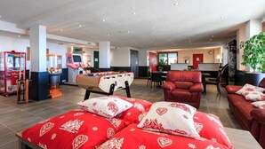 A spacious hotel lobby with a foosball table, red sofas, and a reception desk. - 4-person apartment Hauteurs Super Besse - Indoor pool & Garage (Besse-et-Saint-Anastaise)
