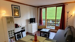 A compact living space with a dining table, a sofa, a TV, and a bookshelf. - 4-person apartment Hauteurs Super Besse - Indoor pool & Garage (Besse-et-Saint-Anastaise)