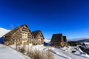 Een hotel in chaletstijl met meerdere balkons en een piste op de achtergrond.