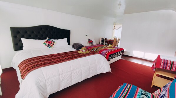 Un dormitorio con una cama grande, una cama más pequeña, una silla de madera y una mesa con sillas.