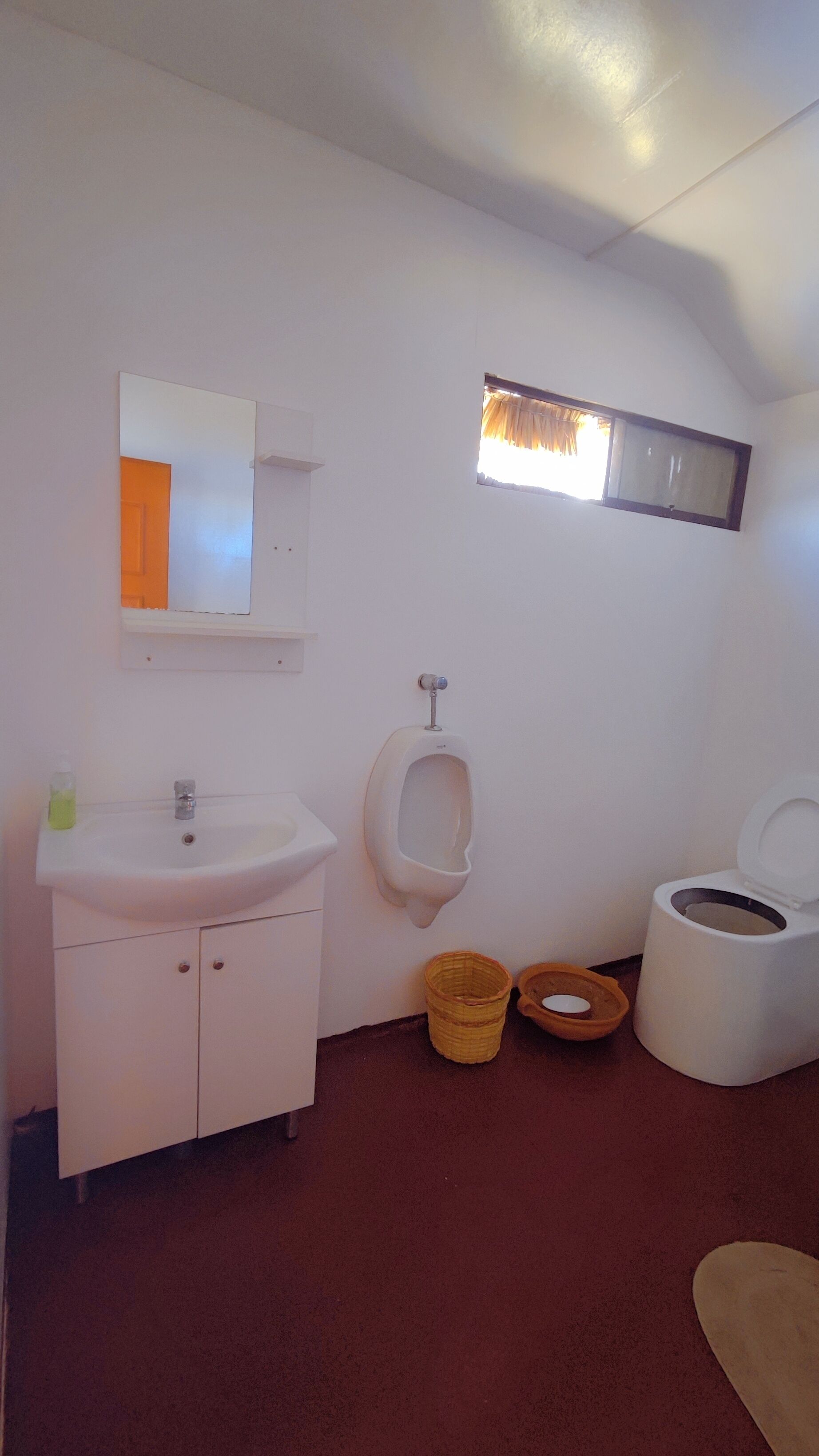 Ein Badezimmer mit Waschbecken, Urinal, Toilette und einem kleinen Fenster.