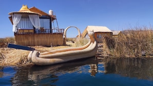 A traditional boat docked near a thatched-roof building with a water tank on the roof. - Room with Panoramic view in the Uros - Lake Titicaca (Puno)