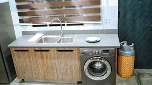 A compact kitchen with a sink, a dish rack, a washing machine, and a trash bin. - Immaculate 3-bed Apartment in Accra (North Legon)
