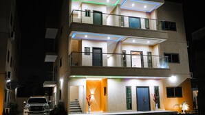 A multi-story building with a modern design, featuring balconies, a staircase, and illuminated entryways. - Immaculate 3-bed Apartment in Accra (North Legon)