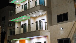 A multi-story building with balconies, a flat roof, and a well-lit entrance. - Immaculate 3-bed Apartment in Accra (North Legon)