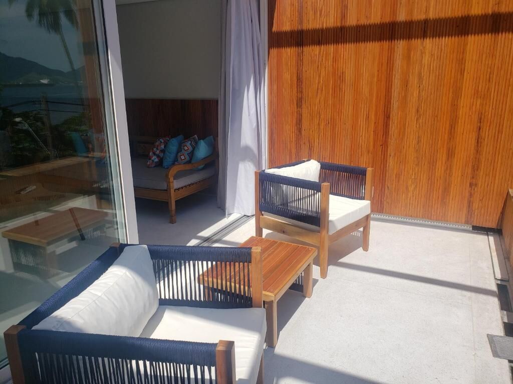 A balcony with wooden furniture, including a sofa and chairs, and a view of the outdoors.