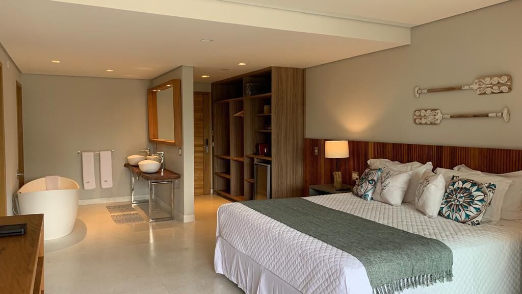 A modern hotel room with a large bed, a vanity with a sink, a walk-in closet, and a wooden headboard.
