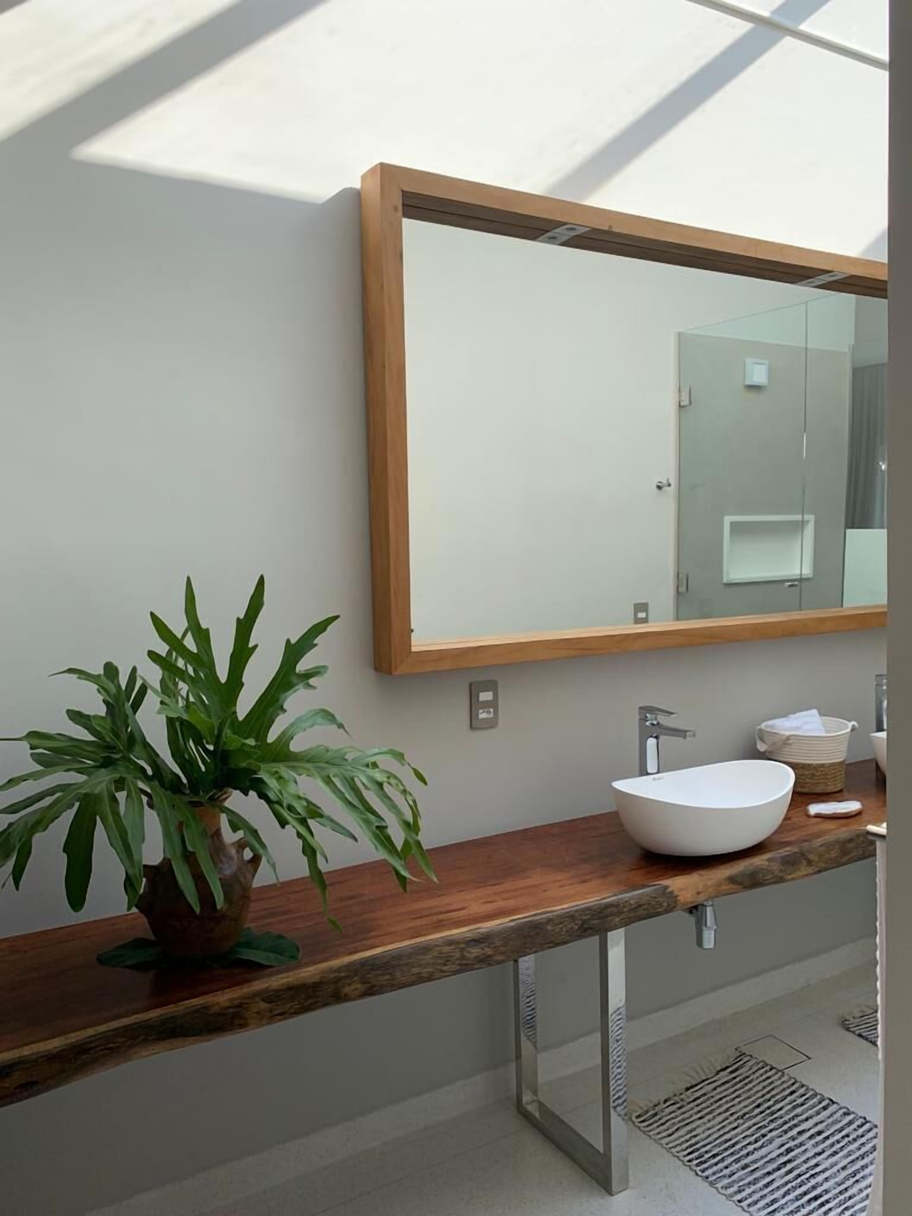 Uma casa de banho moderna com um móvel de vaidade em madeira, um espelho grande e uma planta em vaso.