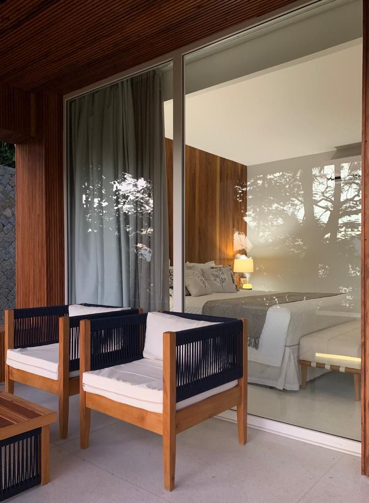 Quarto com uma grande porta de vidro deslizante que dá para uma varanda, uma cama com mesa de cabeceira e uma cadeira com almofada.