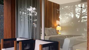 Quarto com uma grande porta de vidro deslizante que dá para uma varanda, uma cama com mesa de cabeceira e uma cadeira com almofada.