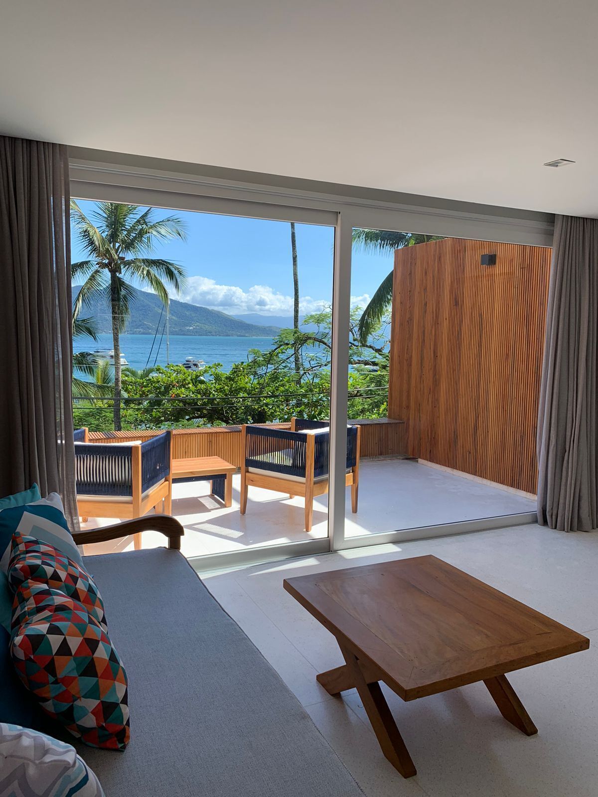 A modern room with a large sliding glass door leading to a balcony with a view of the ocean and palm trees.