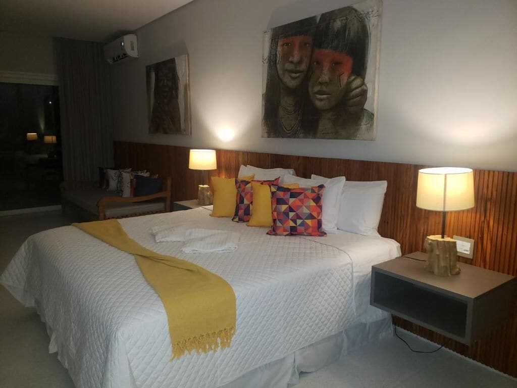 A hotel room with a bed, two bedside lamps, a TV, and artwork on the walls.