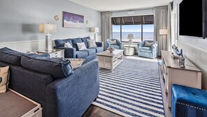 A modern living room with a sofa, armchairs, a coffee table, and a view of the ocean through large windows. - Updated oceanfront condo w/pool, great location near Main St and other attractions (North Myrtle Beach)