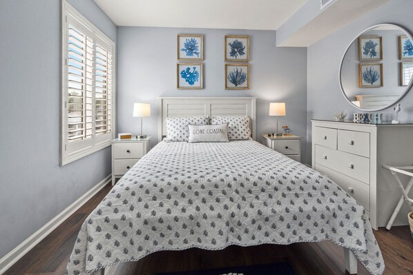 A bedroom with a bed, two bedside tables, a dresser, a mirror, and framed artwork on the wall. - Updated oceanfront condo w/pool, great location near Main St and other attractions (North Myrtle Beach)