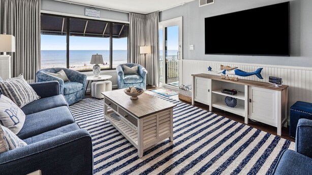 A modern living room with a large TV, comfortable seating, a view of the ocean, and a wooden coffee table. - Updated oceanfront condo w/pool, great location near Main St and other attractions (North Myrtle Beach)