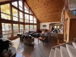 A spacious living area with large windows, a wooden ceiling, and a cozy seating arrangement.
