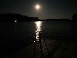 Un moll de fusta s'estén sobre l'aigua de nit, amb una lluna plena que es reflecteix a la superfície.