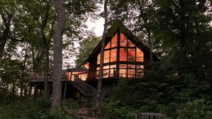Een chalet met een houten trap naar een terras, omgeven door een dicht bos.