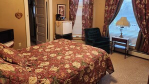 Ein Schlafzimmer mit floralem Bettbezug, einem Schreibtisch mit Lampe, einem Stuhl und einem Kühlschrank.