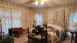Ein Schlafzimmer mit Bett, Schreibtisch, Stuhl, einem kleinen Tisch und einem Deckenventilator.